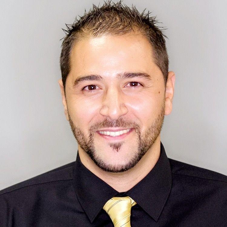 Person wearing a black shirt with a golden tie, short spiky hair visible.